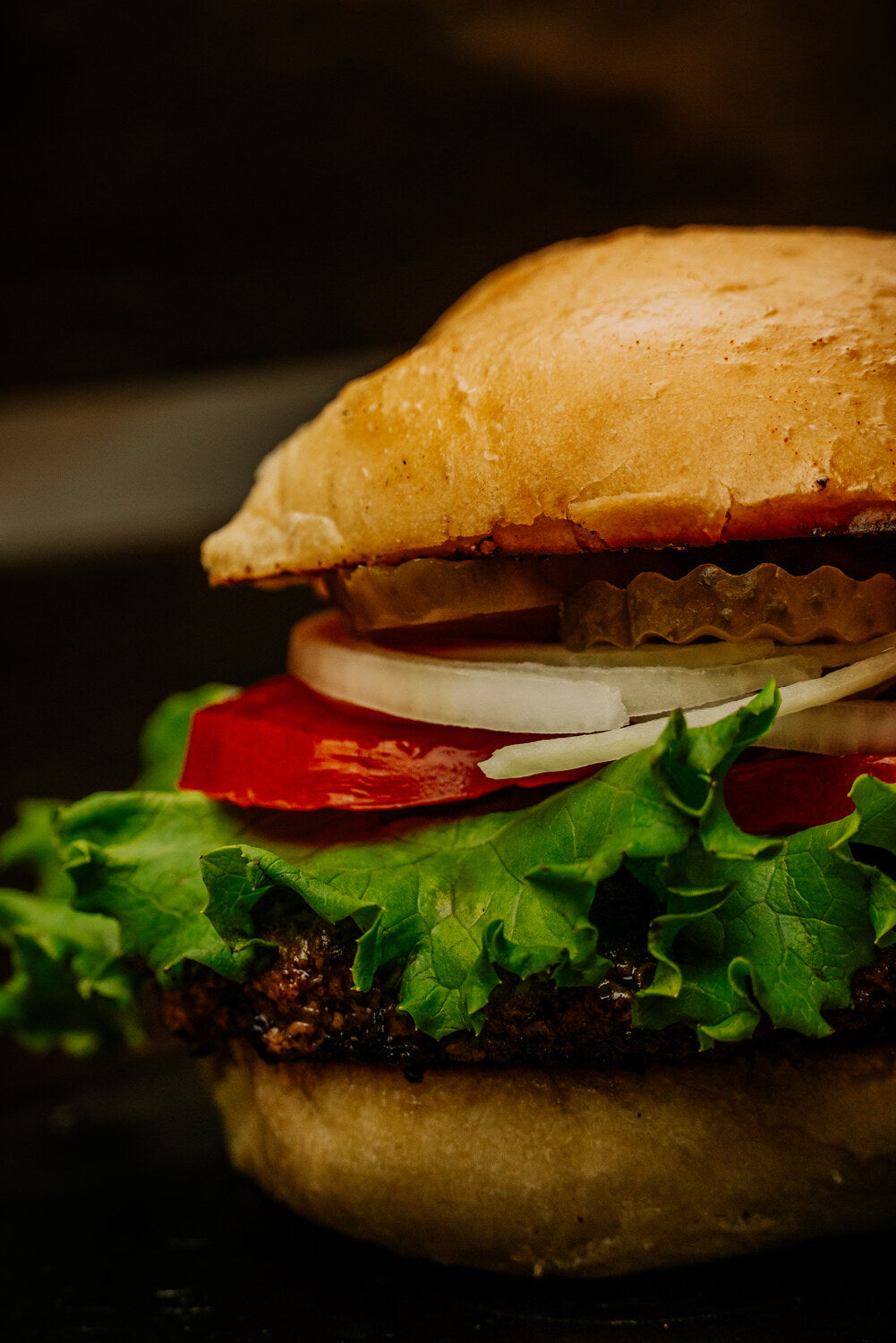 A close-up of a 5L burger with lettuce, tomato, onion and pickles